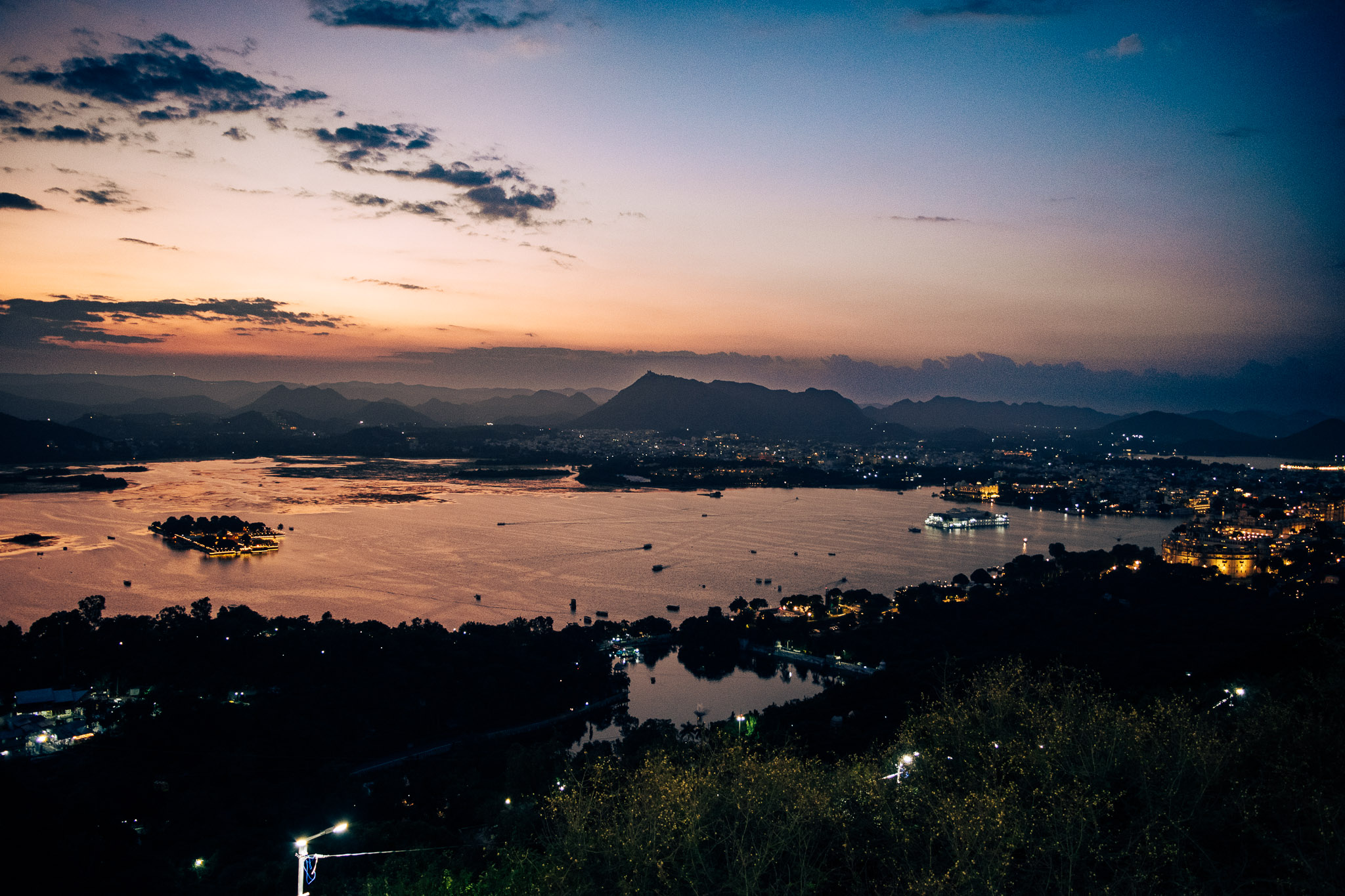 Udaipur lake at blue hour after sunset with calm water and city lights.